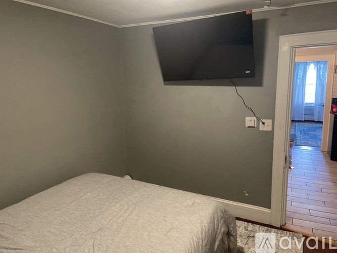 A bedroom with a bed, a flat screen TV mounted on the wall, and a door leading to a hallway.