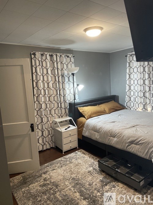 A bedroom with a bed, nightstand, and window with curtains.