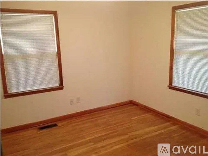 A room with wooden floors and two windows with blinds.