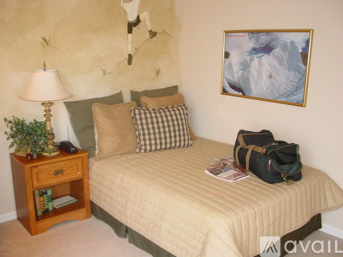 A bedroom with a bed, a lamp, a backpack, and a painting on the wall.