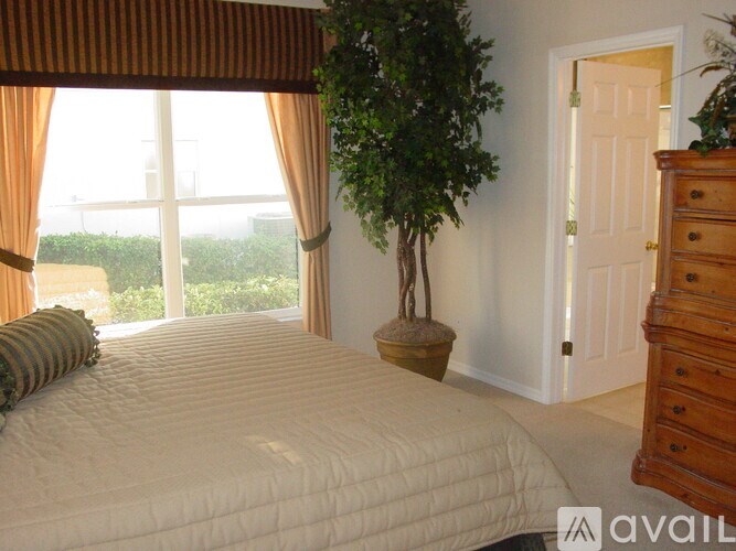 A bedroom with a large bed, a dresser, and a window with curtains.