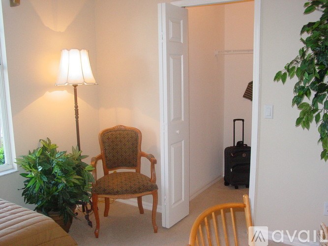 A lamp with a white shade stands next to a chair in a room.
