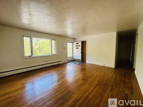 A room with wooden floors and white walls, with a door on the right and two windows on the left.