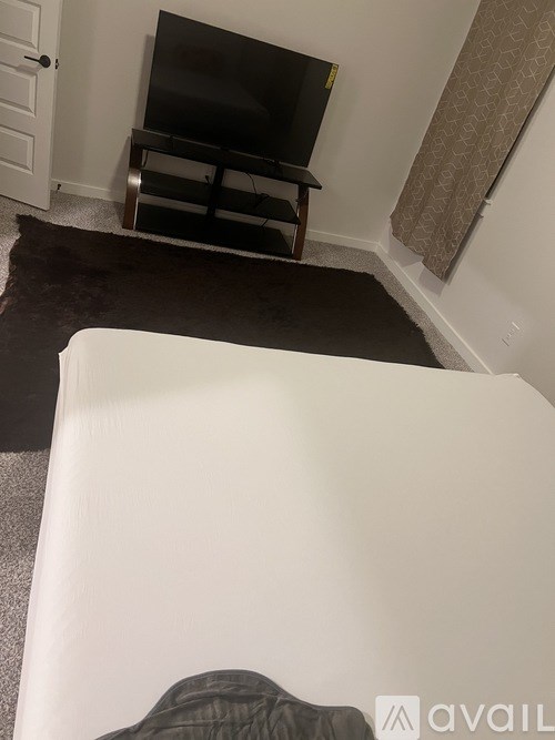 A white bed with a black pillow is in the foreground of a room with a television and a door.