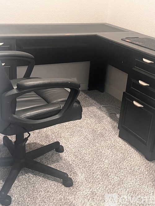 A black office chair is in front of a black desk with drawers.