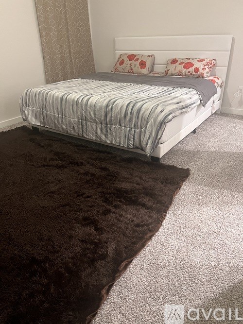 A bed with a white headboard and a striped comforter is in a room with a brown rug.