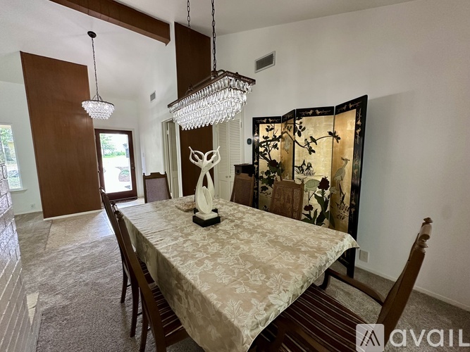 A dining room with a table set for two and a chandelier hanging from the ceiling.