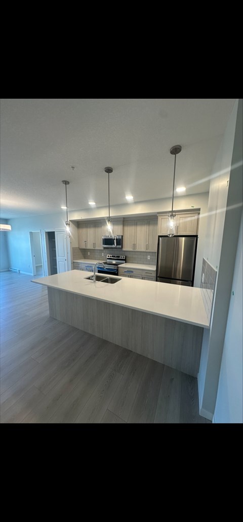 A modern kitchen with a long counter and pendant lights.