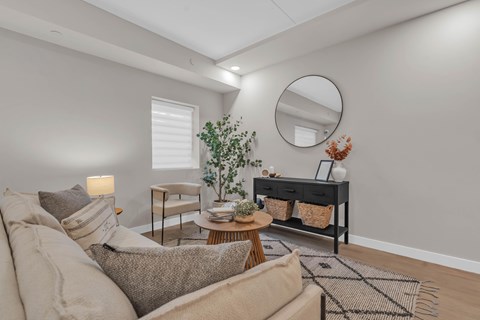 A living room with a beige sofa, a round mirror, and a wooden coffee table.