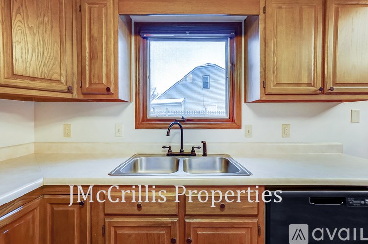 A kitchen with wooden cabinets and a window overlooking a house.