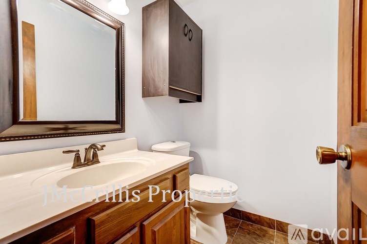 A bathroom with a toilet, sink, mirror and cabinet.