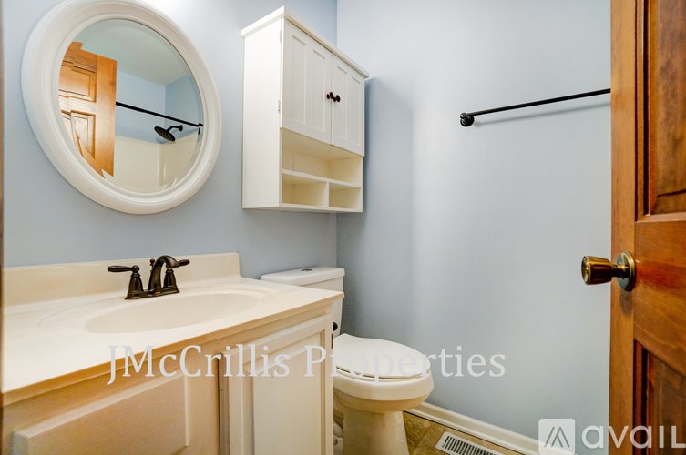 A bathroom with a round mirror, sink, toilet and medicine cabinet.