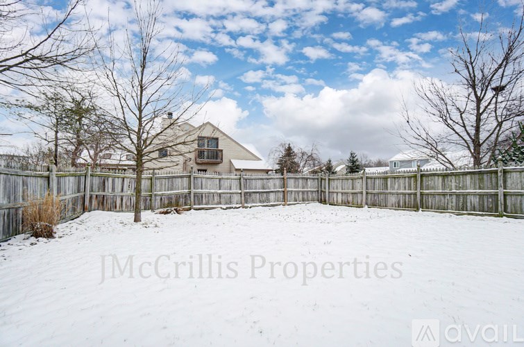 A snow-covered yard with a house and a fence in the background.