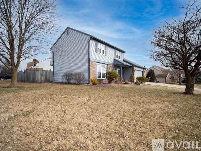 A grey house with a white fence and trees in the background.