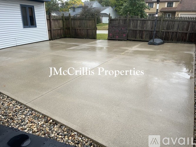 A wet concrete backyard with a fence and a house in the background.