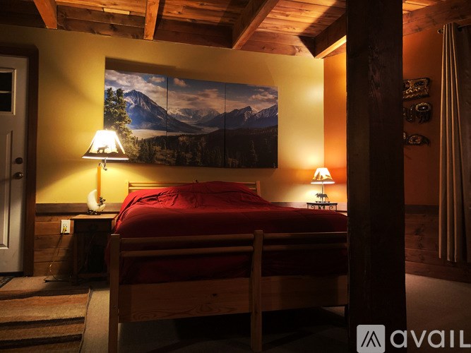 A bedroom with a bed, two lamps, and a mountain painting on the wall.
