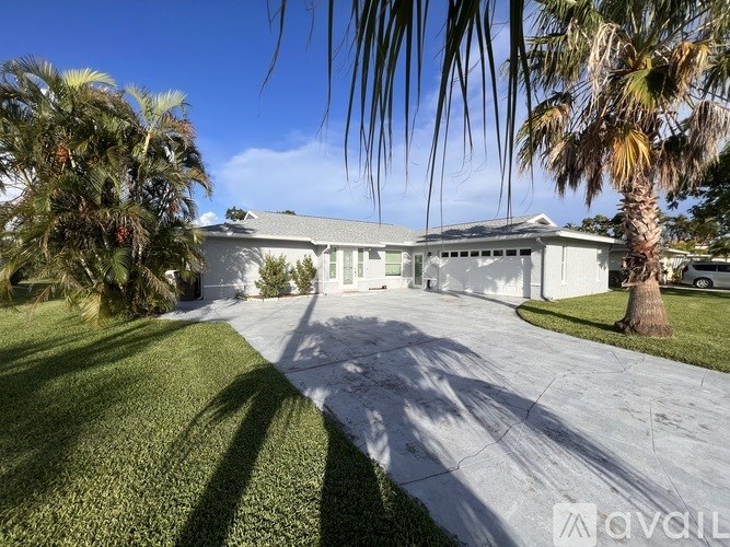 A white house with a driveway and palm trees in front.