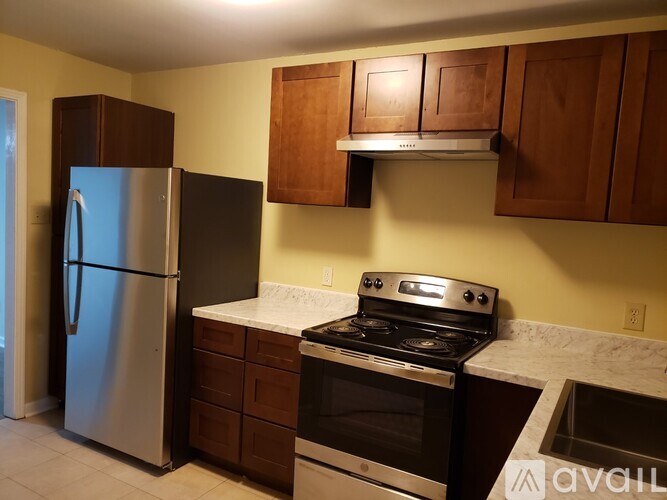 A kitchen with a stainless steel refrigerator, a stove, and wooden cabinets.