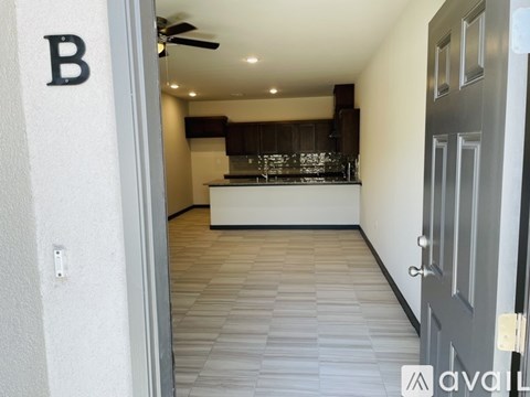 A hallway with a door on the right and a kitchen area visible through the door.