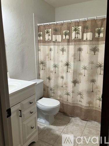 A bathroom with a toilet, sink, and a shower curtain with palm trees on it.