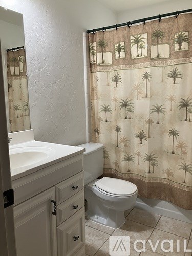 A bathroom with a toilet, sink, and a shower curtain with palm trees on it.