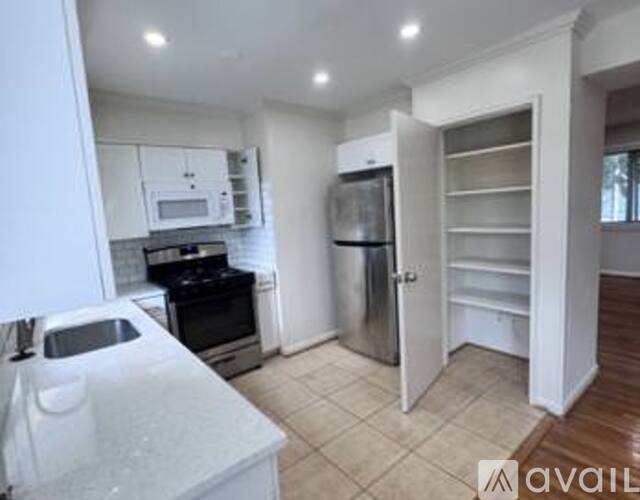 A kitchen with white cabinets and appliances, a white island, and a white door leading to another room.