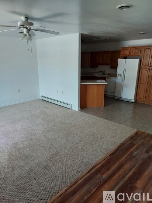 A room with a ceiling fan and a kitchen area in the background.