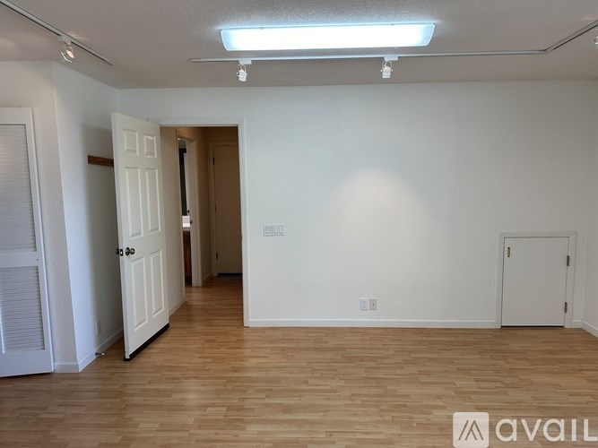 A room with wooden floors and white walls, with a door on the left and another door on the right.