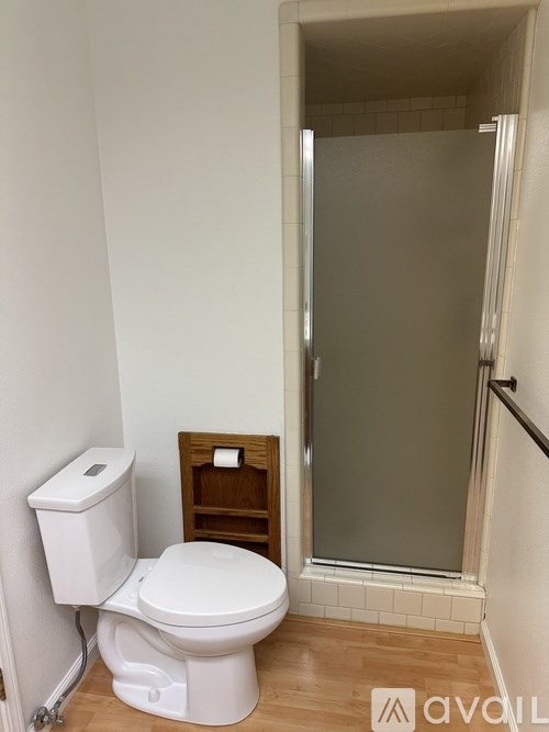 A white toilet with a white tank and a white shower stall.