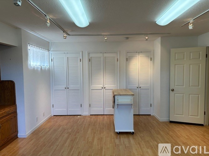 A room with white walls and wooden flooring, featuring a white cabinet and a white door.