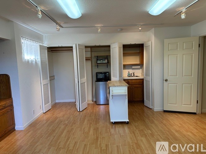 A kitchen area with a white fridge, wooden floors, and white walls.