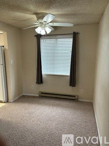 A room with a carpeted floor, a ceiling fan, and a window with blinds.