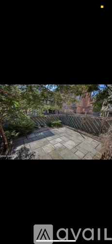 A view of a courtyard surrounded by a fence with trees and a building in the background.