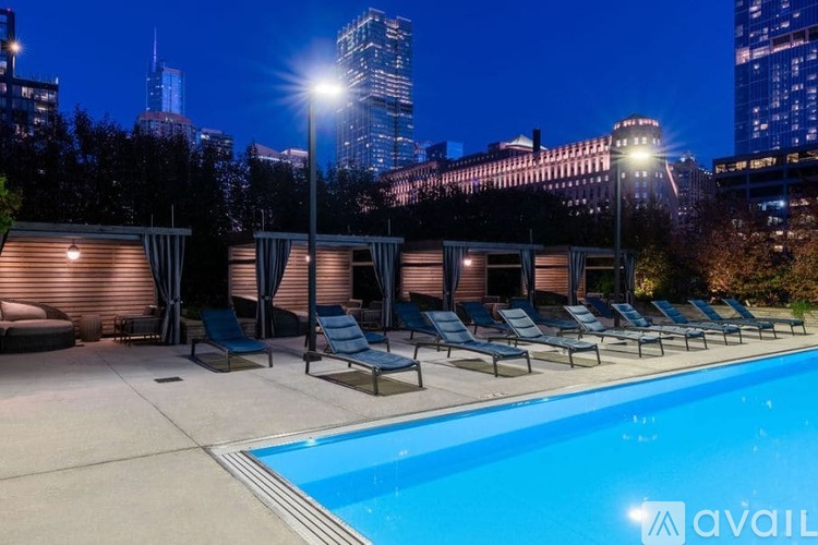 A pool area with lounge chairs and a city skyline at night.