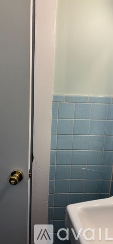A white door with a gold knob is open to a blue tiled bathroom.