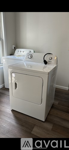 A white washing machine is placed in a room with wooden flooring.