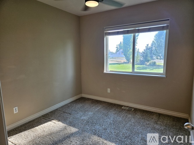 A room with a carpet floor and a window showing a view of a house and trees.