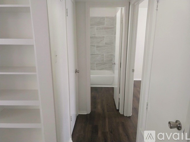 A hallway with a white door and a white shelving unit on the left.