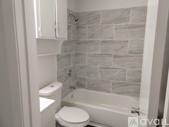 A bathroom with a toilet, a tub, and a wall of tiles.