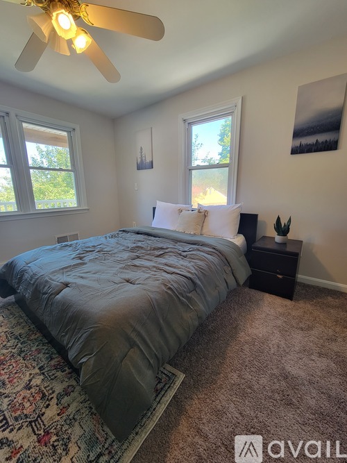 A bedroom with a bed, a ceiling fan, and two windows.