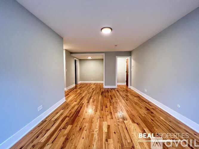 A room with wooden floors and white walls, with a doorway leading to another room.