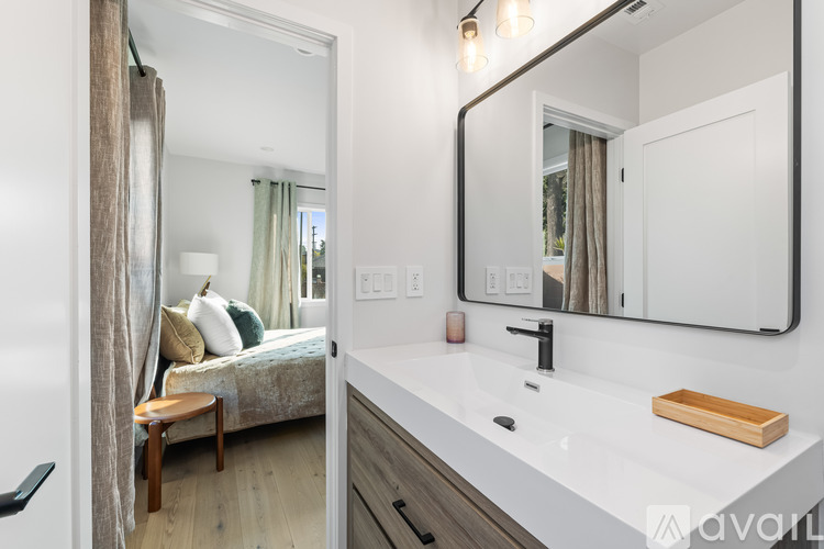 A modern bathroom with a large mirror and a bedroom area visible through the mirror.
