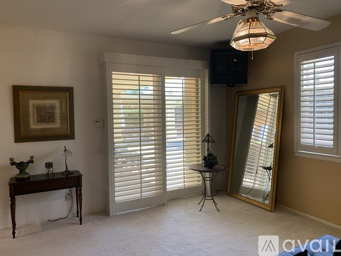 A room with a ceiling fan, a table with a vase and candle, a mirror, and a painting on the wall.