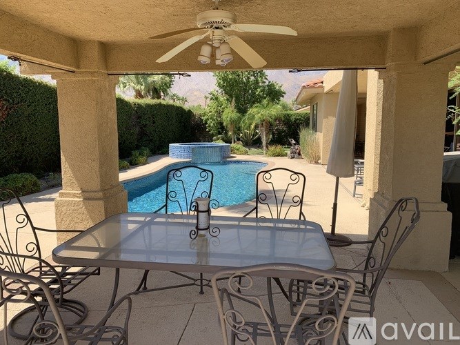 A patio with a table and chairs overlooking a pool.