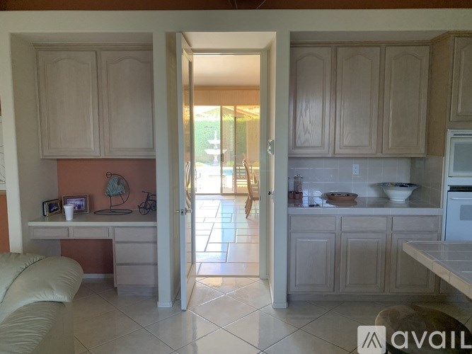 A kitchen with a desk and chair in the foreground and a doorway leading to a dining area.