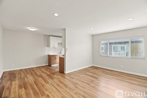 A spacious room with wooden flooring and a kitchen area in the background.