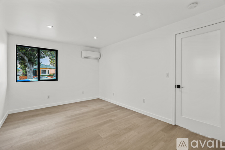 A room with a white door and a window with a view of a building and trees.