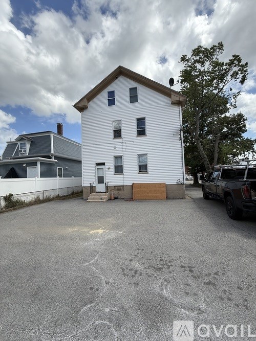 A white house with a grey roof and a tree in front of it.