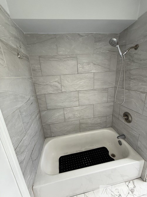 A white bathtub with a black mat in a bathroom with grey tiles.