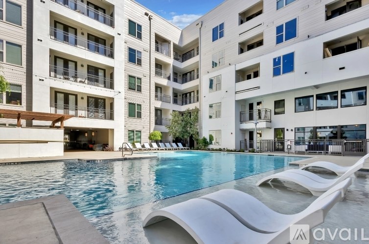 A modern apartment complex with a pool and lounge chairs.